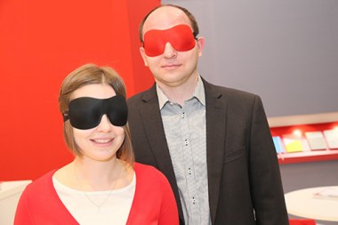 Links: junge Frau mit schwarzer Augenmaske.  Rechts: Mann mit roter Augenmaske. Beide lächeln, die Frau ein wenig mehr.